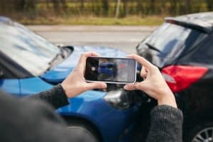 Close-up of woman driver photographing car accident scene with mobile phone for insurance claim documentation.