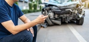 Man calling with phone to his insurance agent after traffic accident with a background of the crashed car, Car insurance an non-life insurance concept.