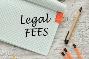 The text 'LEGAL FEES' written on a notebook corner, with orange pencils and a pen nearby, conveying a business theme.