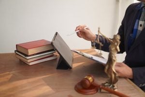 Lawyer at desk reviewing documents with statue of justice, gavel, and books nearby.
