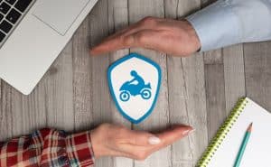 Motorcycle accident cases Hands framing a motorcycle insurance icon on a table with laptop and notebook.