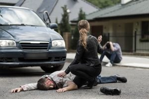 Injured individual from vehicular incident lying on the pavement with visible bloodstains.