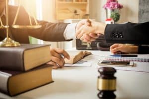  Two professionals shaking hands over a desk with legal books, scales, and a gavel.